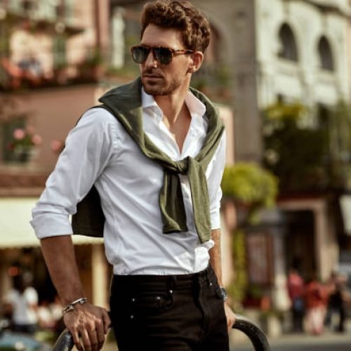 Stylish man wearing sunglasses and white shirt with tied sweater on shoulders